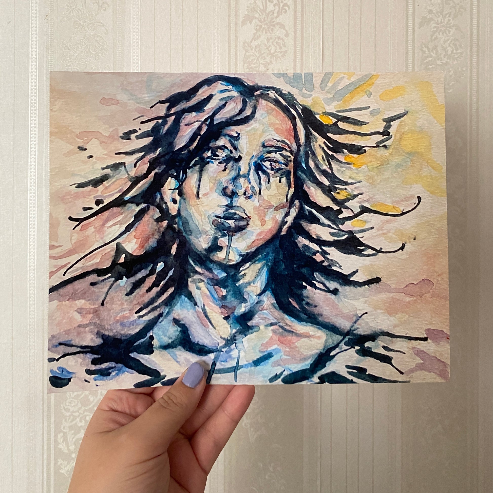 Hand holding a painting of a woman with flowing hair against a textured wall.