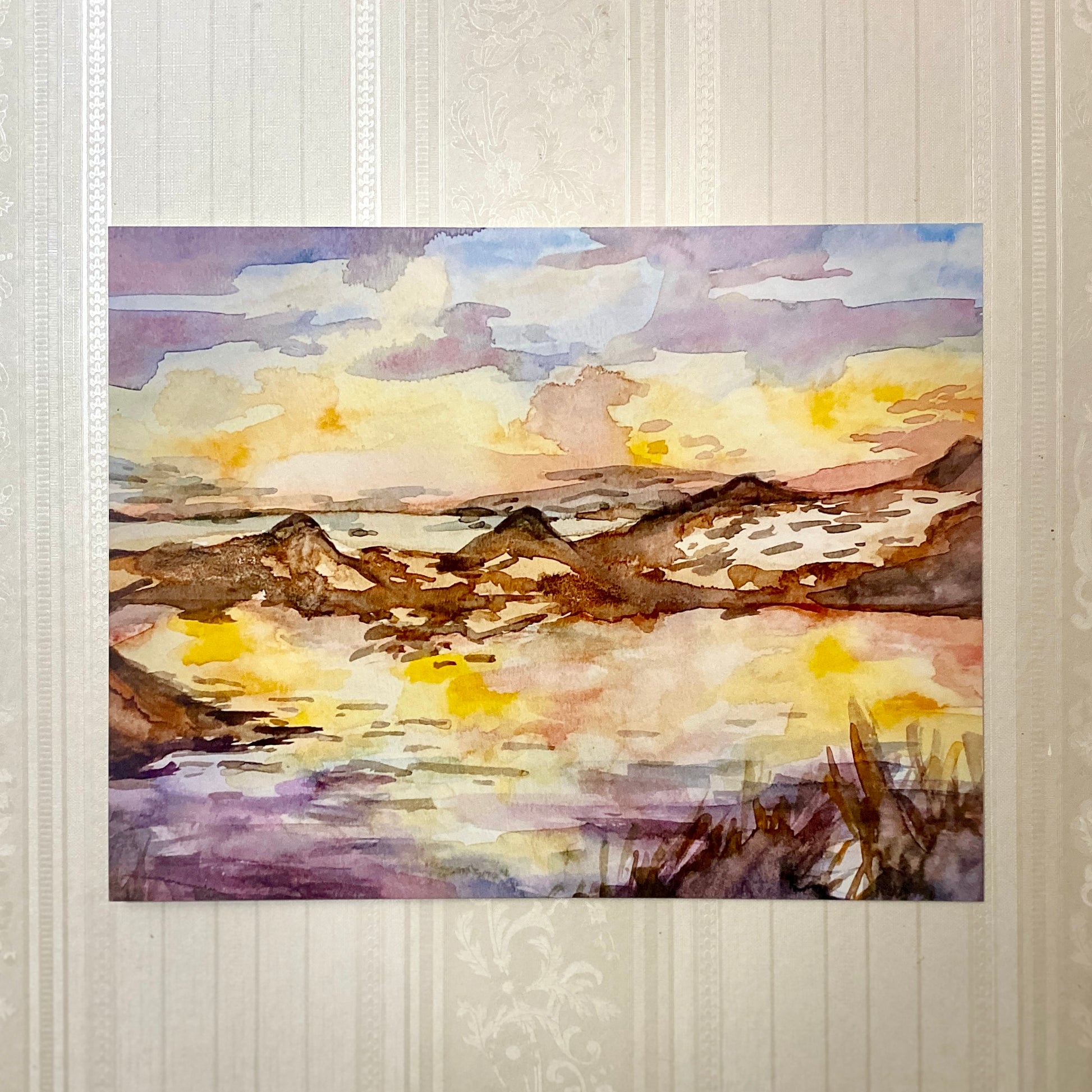 Watercolor painting of a landscape with mountains and a sunset on a textured wall.